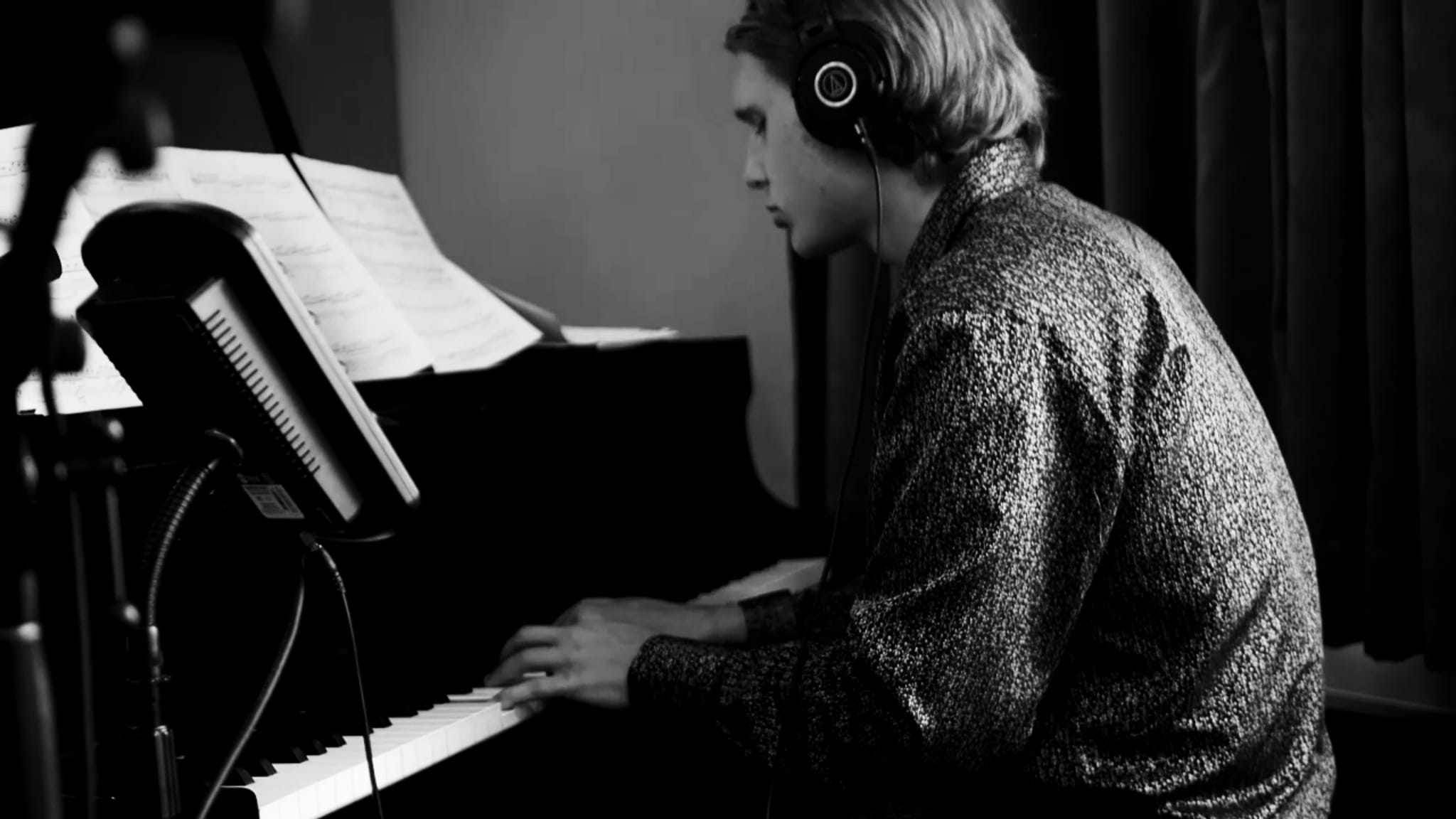 Black-and-white photo of Abe wearing headphones, playing a piano in the studio